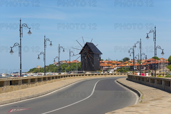 A tidy coastal road leads to a traditional windmill under a bright blue sky, Historic windmill on the causeway, Landmark, Black Sea, Nesebar, Nessebar, Burgas, Bulgaria, Europe