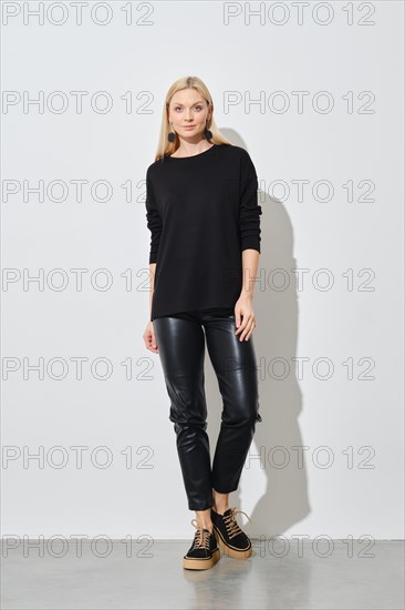 Trendy woman in black pullover and leather trousers posing in bright studio