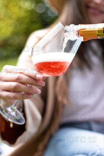 Vertical image of unrecognizable woman holding a glass cup while being served some red champagne outdoors in the park
