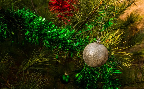 Silver textured Christmas ornament and green tensile garland hanging on pine tree in local park in South Korea