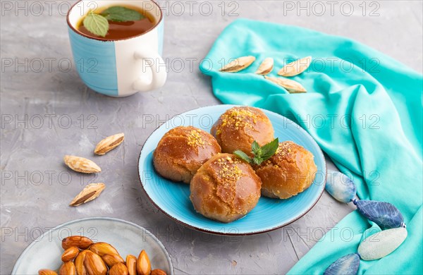 Homemade traditional turkish dessert sekerpare with almonds and honey, cup of green tea on gray concrete background and blue textile. side view