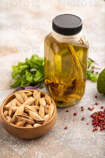 Sunflower oil in a glass jar with various herbs and spices, sesame, rosemary, avocado, basil, almond on a brown concrete background. Side view, selective focus, close up