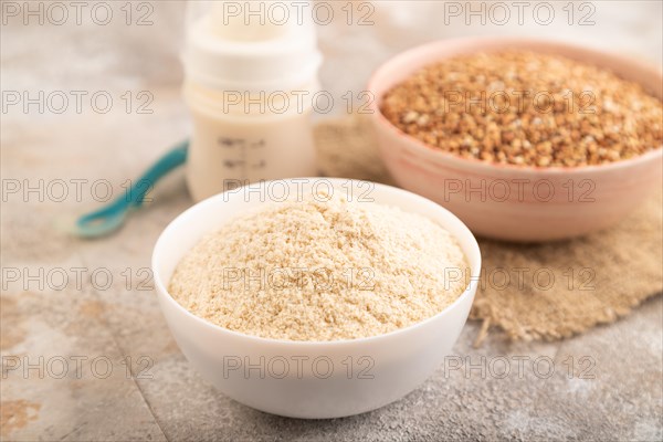 Powdered milk and buckwheat baby food mix, infant formula, pacifier, bottle, spoon on brown concrete background and linen textile. Side view, close up, selective focus, artificial feeding concept