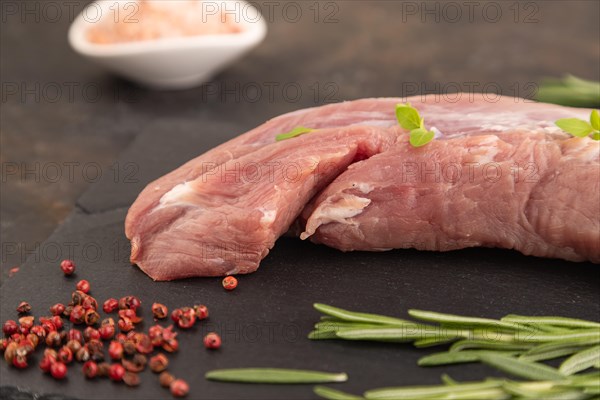 Raw pork meat with herbs and spices on slate cutting board on black concrete background. Side view, close up, selective focus