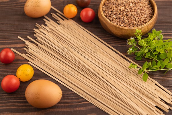Japanese buckwheat soba noodles with tomato, eggs, spices, herbs on brown wooden background. Side view, close up, selective focus
