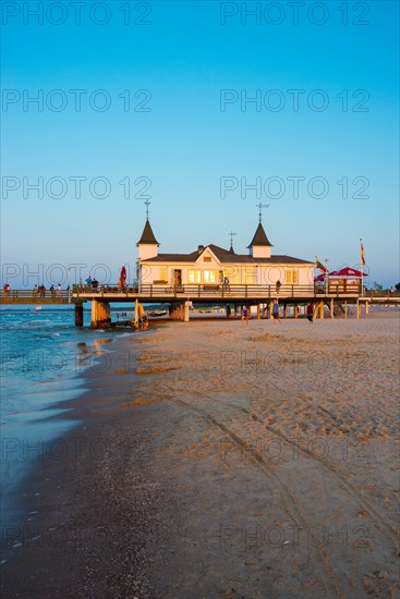 People strolling on a pier with buildings in the sunset, clear, blue, cloudless sky, pier Ahlbeck in the last sunlight, view from the western beach to the east, seaside resort Ahlbeck, island Usedom, Mecklenburg-Western Pomerania, Germany, Europe