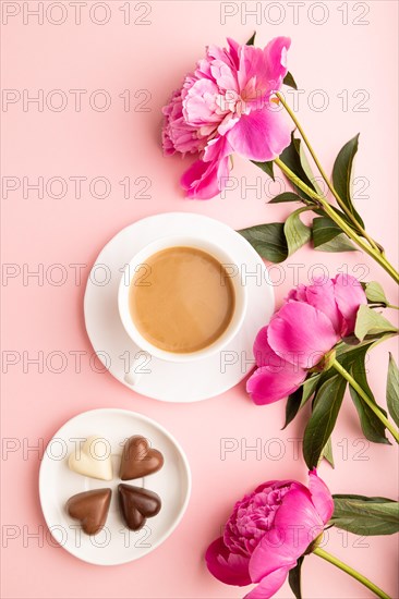 Cup of cioffee with chocolate candies, pink peony flowers on pink pastel background. top view, flat lay, close up, still life. Breakfast, morning, spring concept