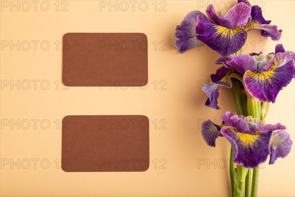 Brown business card with lilac iris flowers on orange pastel background. top view, flat lay, copy space, still life. Breakfast, morning, spring concept