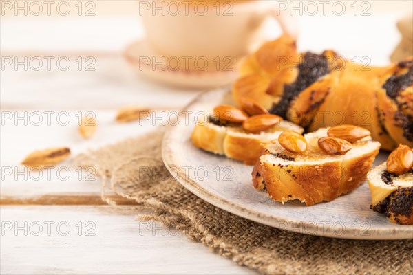 Homemade sweet bun with honey almonds and cup of green tea on a white wooden background and linen textile. side view, close up, selective focus