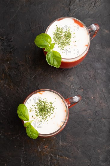 Tomato juice with basil and sour cream in glass on a black concrete background. Healthy drink concept. Top view, flat lay, close up