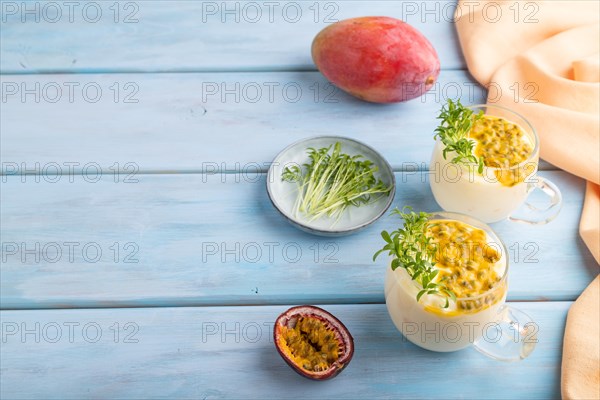 Mango yogurt with passionfruit and cilantro microgreen in glass on blue wooden background with orange linen textile. Side view, copy space
