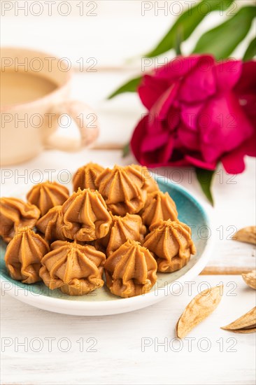 Homemade soft caramel fudge candies on blue plate and cup of coffee on gray concrete background, peony flower decoration. side view, close up, selective focus