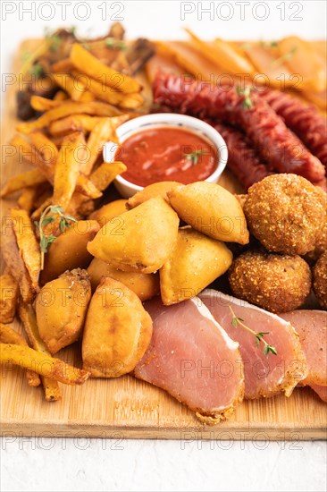 Set of snacks: sausages, fried potatoes, meat balls, dumplings, basturma on a cutting board on a gray concrete background. Side view, close up, selective focus