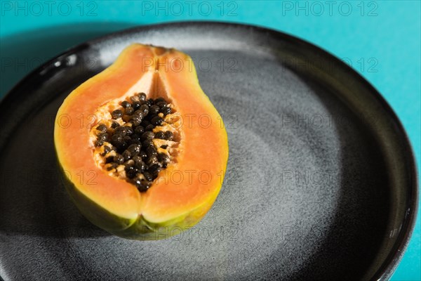 Ripe cut papaya on gray plate on blue pastel background. Side view, close up, hard light. Tropical, healthy food, women health concept, minimalism