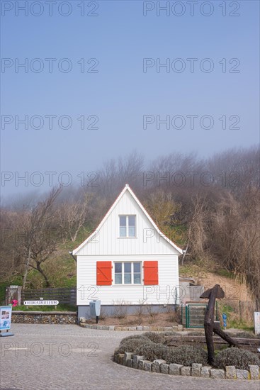 Old, white wooden house with red shutters stands in the fog, old anchor, sea fog, wind fugitive, village Kloster, island Hiddensee, Baltic Sea, Germany, Europe