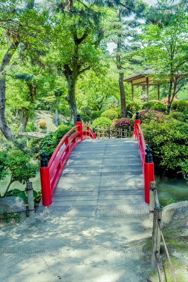 Red wooden footbridge over man made pond in Japanese garden in Hiroshima, Japan, Asia