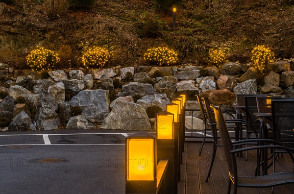 Yellow lights on patio banister with small evergreen shrubs decorated with Christmas lights in background in South Korea