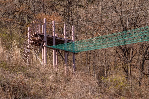 Fire brigade training tower and attached safety net used to practice balance located in mountainside with blue sky with puffy white clouds in background