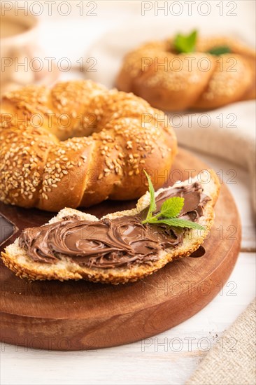 Homemade sweet bun with chocolate cream and cup of coffee on a white wooden background and linen textile. side view, close up, selective focus