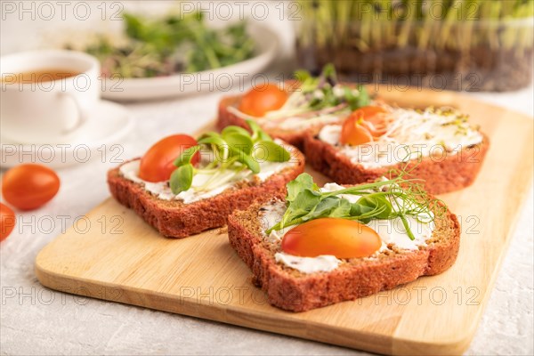 Red beet bread sandwiches with cream cheese, tomatoes and microgreen on gray concrete background. side view, close up, selective focus