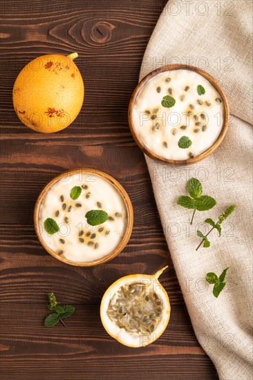 Yoghurt with granadilla and mint in wooden bowl on brown wooden background and linen textile. top view, flat lay, close up