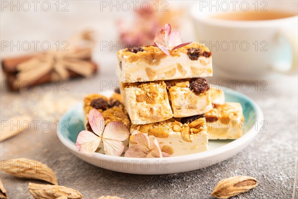 Traditional candy nougat with nuts and sesame with cup of green tea on brown concrete background. side view, close up, selective focus