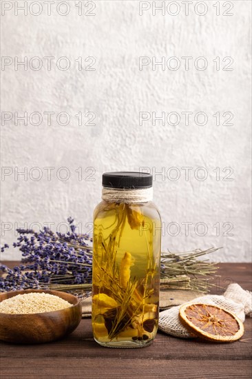 Sunflower oil in a glass jar with various herbs and spices, lavender, sesame, rosemary on a brown wooden background. Side view, copy space