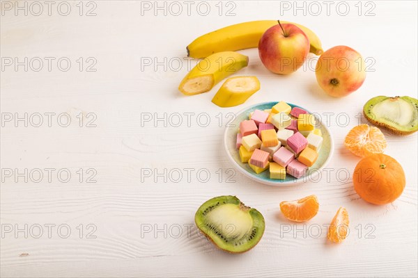 Various fruit jelly chewing candies on plate on white wooden background. apple, banana, tangerine, kiwi, side view, copy space