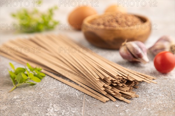 Japanese buckwheat soba noodles with tomato, eggs, spices, herbs on brown concrete background. Side view, close up, selective focus