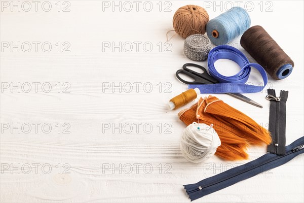 Sewing accessories: scissors, thread, thimbles, braid on white wooden background. Side view, copy space