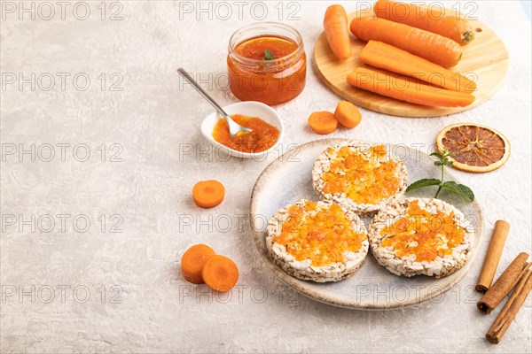 Carrot jam with puffed rice cakes on gray concrete background. Side view, copy space