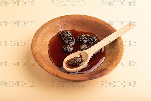 Pine cone jam in wooden bowl on orange pastel background. Side view, close up
