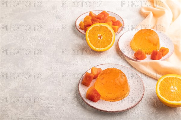 Papaya and orange jelly on gray concrete background and orange linen textile. side view, flat lay, copy space