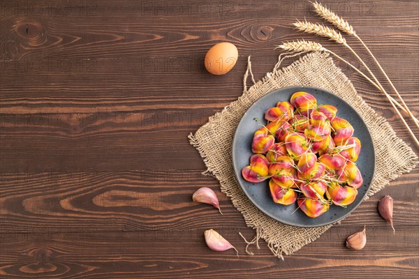 Rainbow colored dumplings with pepper, herbs, microgreen on brown wooden background and linen textile. Top view, flat lay, copy space