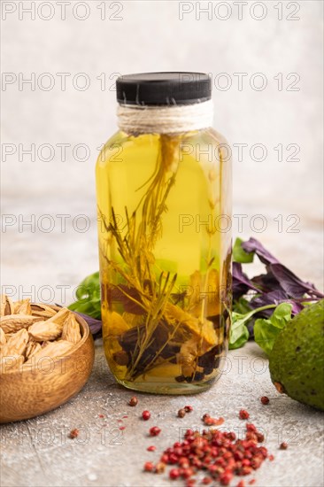 Sunflower oil in a glass jar with various herbs and spices, sesame, rosemary, avocado, basil, almond on a brown concrete background. Side view, selective focus, close up
