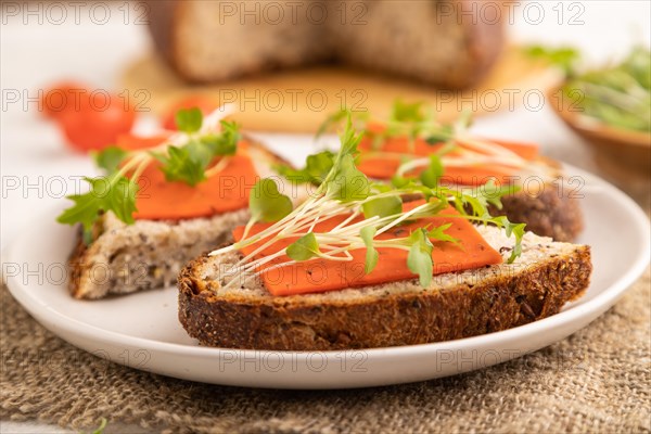 Grain bread sandwiches with red tomato cheese and mizuna cabbage microgreen on gray concrete background and linen textile. side view, close up, selective focus