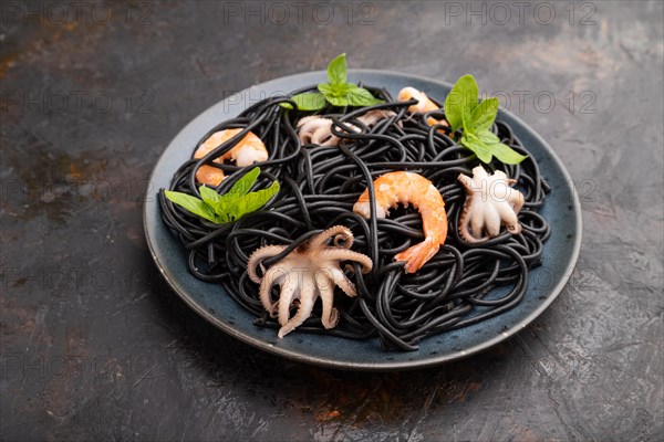 Black cuttlefish ink pasta with shrimps or prawns and small octopuses on black concrete background. Side view, close up