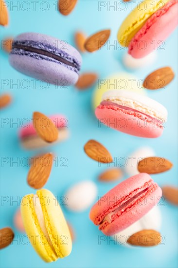 Multicolored flying macaroons and almonds eggs frozen in the air on blurred blue background. top view, flat lay, close up. Breakfast, morning, concept