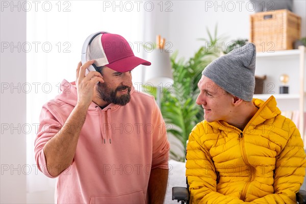 Man listening to music using headphones next to a disabled friend in wheelchair at home