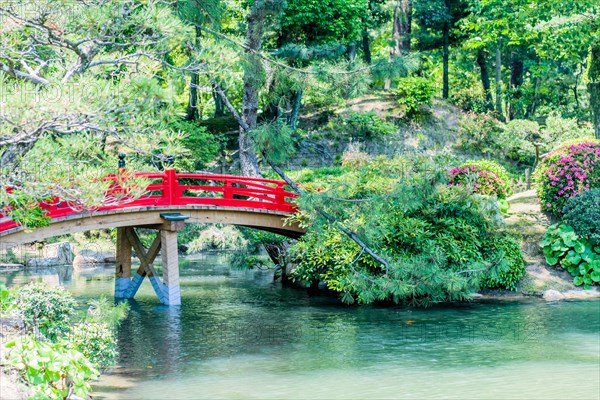 Red wooden footbridge over man made pond in Japanese garden in Hiroshima, Japan, Asia