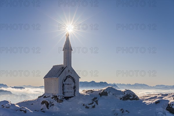 Small chapel with sun star on snowy mountain peak, backlight, winter, chapel on Hochgern, Chiemgau Alps, Upper Bavaria, Bavaria, Germany, Europe