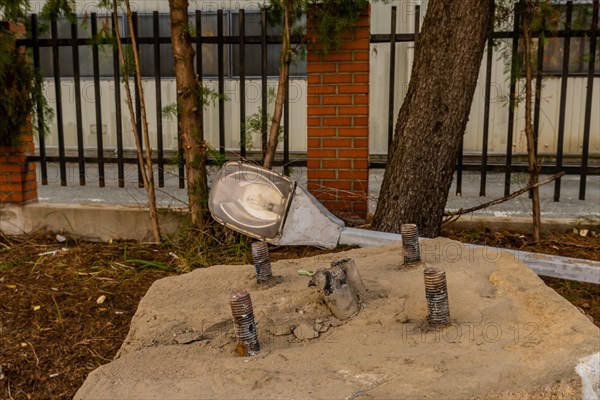 Old dismantled streetlight removed from lamppost and laying on ground behind concrete streetlamp base