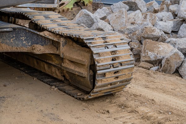 Track assembly of backhoe in front of large pieces if concrete at construction site