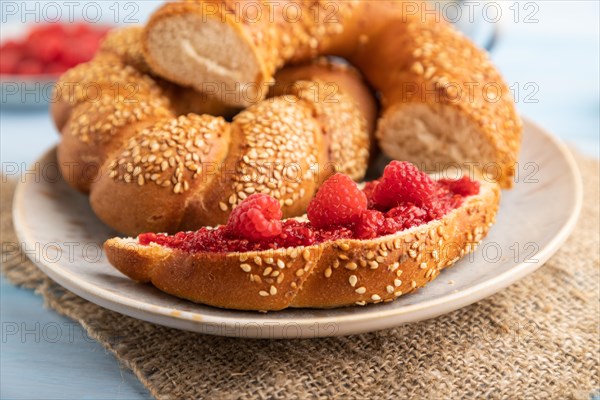 Homemade sweet bun with raspberry jam and cup of coffee on a blue wooden background and linen textile. side view, close up, selective focus