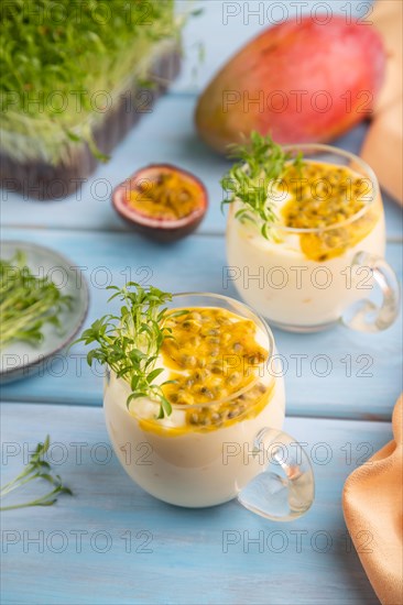 Mango yogurt with passionfruit and cilantro microgreen in glass on blue wooden background with orange linen textile. Side view, close up, selective focus