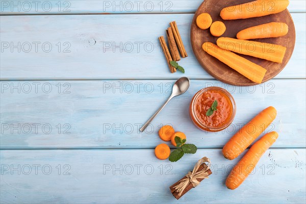 Carrot jam with cinnamon in glass jar on blue wooden background. Top view, flat lay, copy space