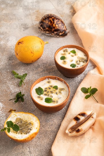 Yoghurt with granadilla and mint in clay bowl on brown concrete background and orange linen textile. side view, close up