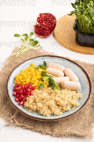 Mixed quinoa porridge, sweet corn, pomegranate seeds and small sausages on white wooden background. Side view, close up. Food for children, healthy food concept