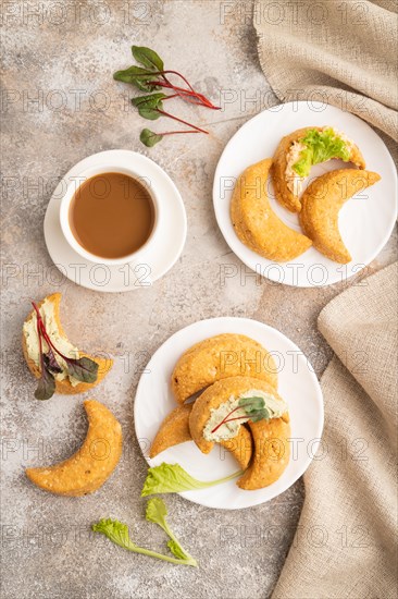 Homemade salted crescent-shaped cheese cookies, cup of coffee on brown concrete background and linen textile. top view, flat lay, close up