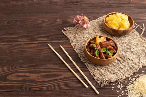 Tteokbokki or Topokki, fried rice cake stick, popular Korean street food with spicy jjajang sauce and pineapple on brown wooden background and linen textile. Side view, copy space
